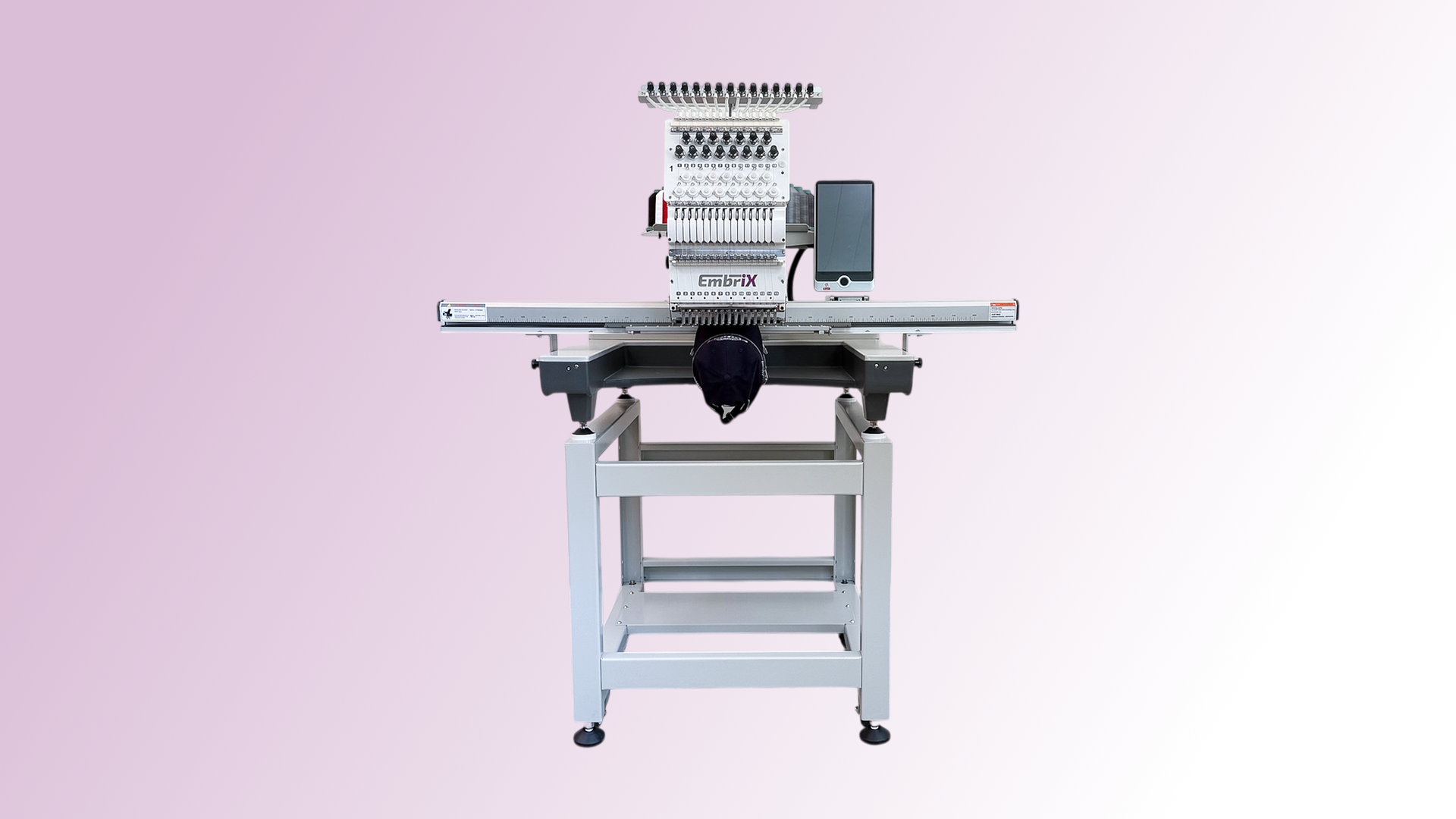 Computergesteuerte EmbrIX Stickmaschine mit Nadelkopf und Bedienfeld auf grauem Metallgestell vor rosa Hintergrund