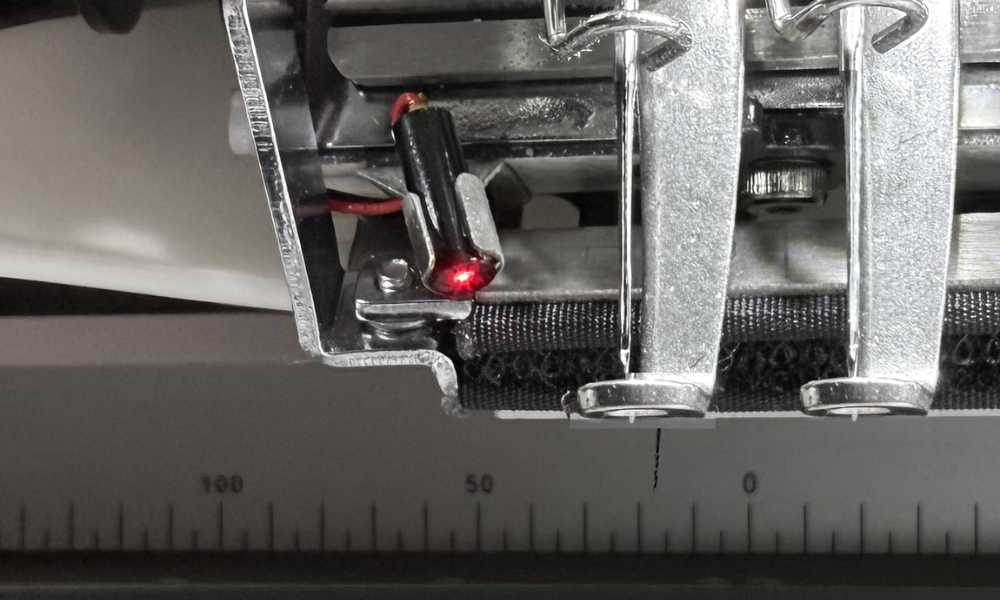 Nahaufnahme einer computergesteuerten Stickmaschine mit Metallrahmen, Nadelhalterung und Maßband bei Null