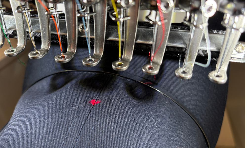 Computergesteuerte Stickmaschine beim Sticken eines roten Motivs auf dunklem Stoff mit mehreren Nadeln und Fäden
