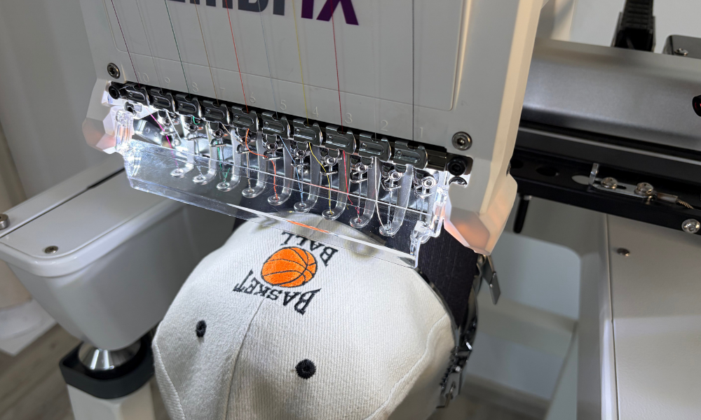 Computergesteuerte Stickmaschine EmbrIX beim Besticken einer weißen Kappe mit Basketball-Logo